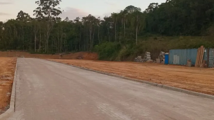 Rua do Loteamento Cidade Jardim II com meio-fio dos dois lados, terra exposta em volta e mata ao fundo.