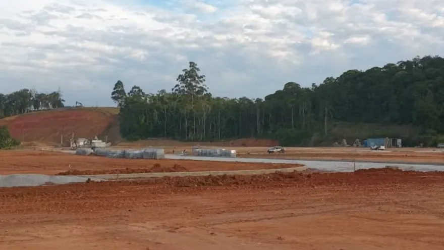 Área do Loteamento Cidade Jardim II com terra exposta, ruas ao fundo e mata.