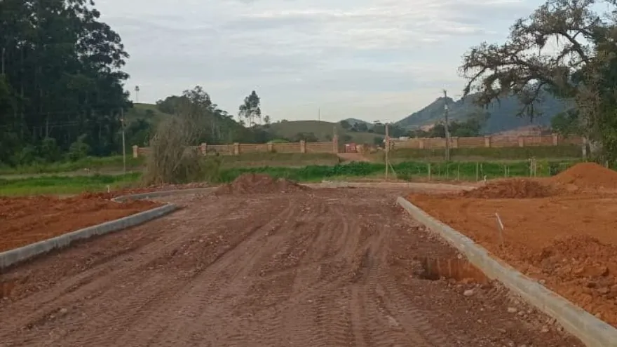 Rua de terra do Loteamento Cidade Jardim II com meio-fio de um lado e árvores ao fundo.