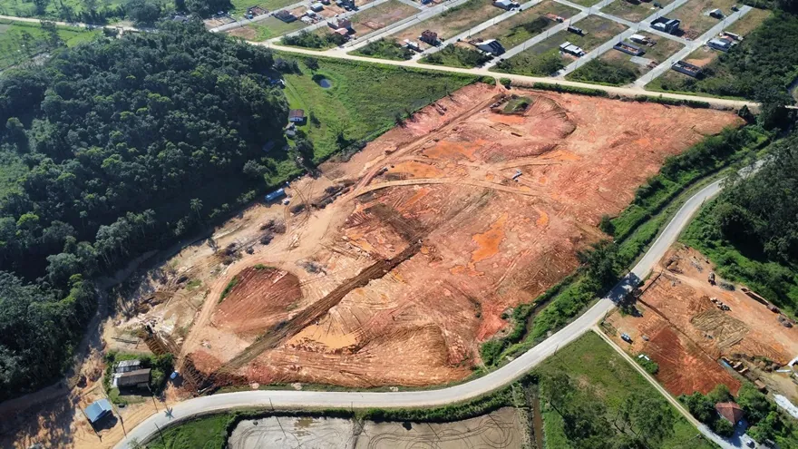 Vista aérea do terreno do Loteamento Cidade Jardim II, de terra exposta, contornado por uma estrada, com mata à esquerda.
