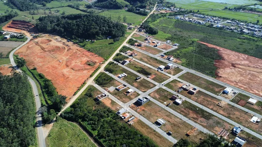 Vista aérea do terreno do Loteamento Cidade Jardim II, de terra exposta, ao lado de ruas com construções.
