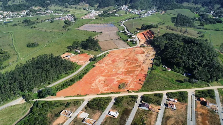 Vista aérea do terreno do Loteamento Cidade Jardim II, de terra exposta, com mata à direita e ruas com construções embaixo.