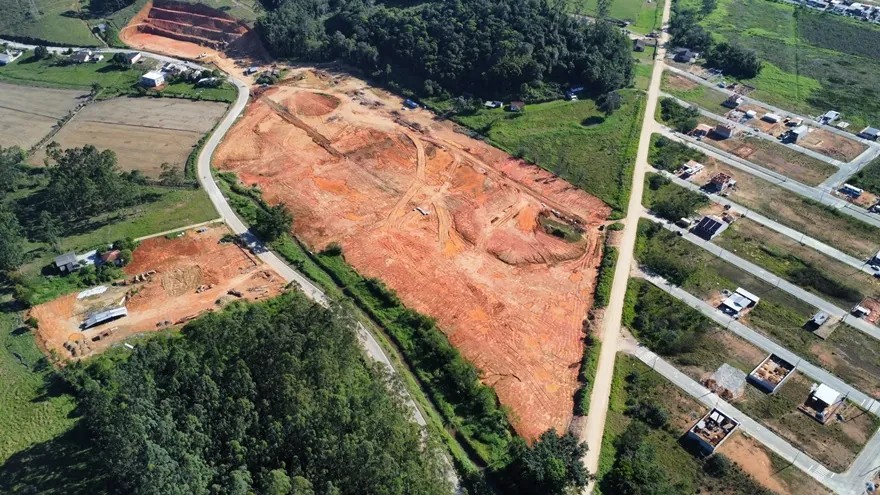 Vista aérea do terreno do Loteamento Cidade Jardim II, de terra exposta, entre uma área de mata e ruas com construções.