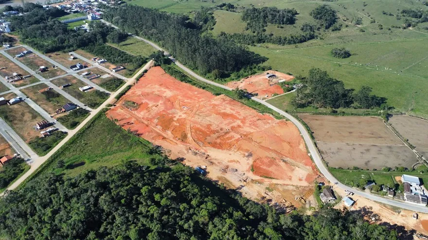 Vista aérea do terreno do Loteamento Cidade Jardim II, de terra exposta, com ruas e construções à esquerda e mata embaixo.