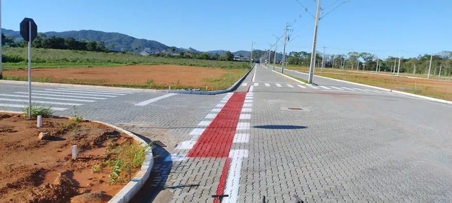 Rua pavimentada do Loteamento Cidade Jardim I, com uma faixa vermelha no piso e postes ao fundo.