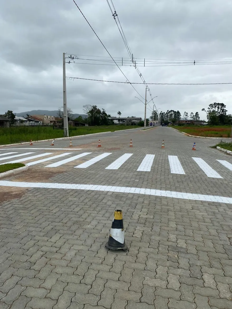 Rua pavimentada do Loteamento Cidade Jardim I, com faixa de pedestres ao fundo e um cone no chão.