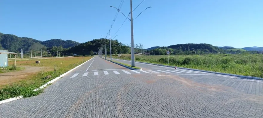 Rua pavimentada do Loteamento Cidade Jardim I vista em linha reta, com postes e morros ao fundo.