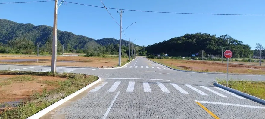Cruzamento de ruas pavimentadas no Loteamento Cidade Jardim I, com faixa de pedestres, postes e placa de pare.