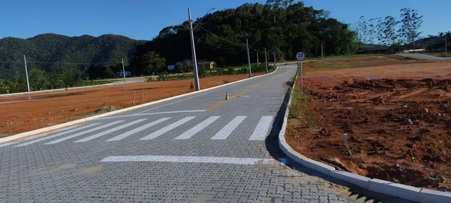 Curva de rua pavimentada no Loteamento Cidade Jardim I, com faixa de pedestres e um lote de terra ao lado.